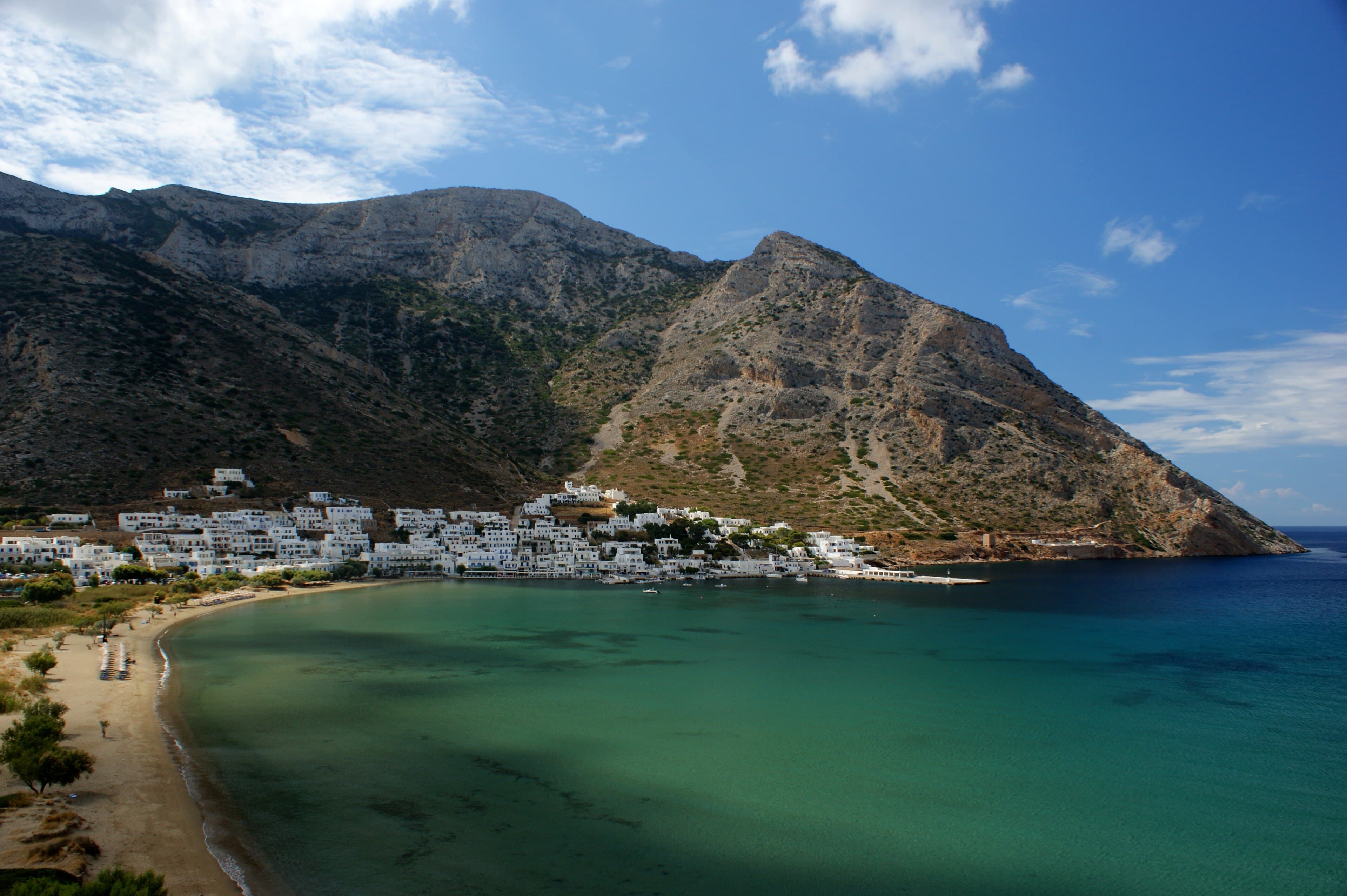 The bay at Kamáres, Sífnos: green water, a white village along the shore, bare mountain behind.