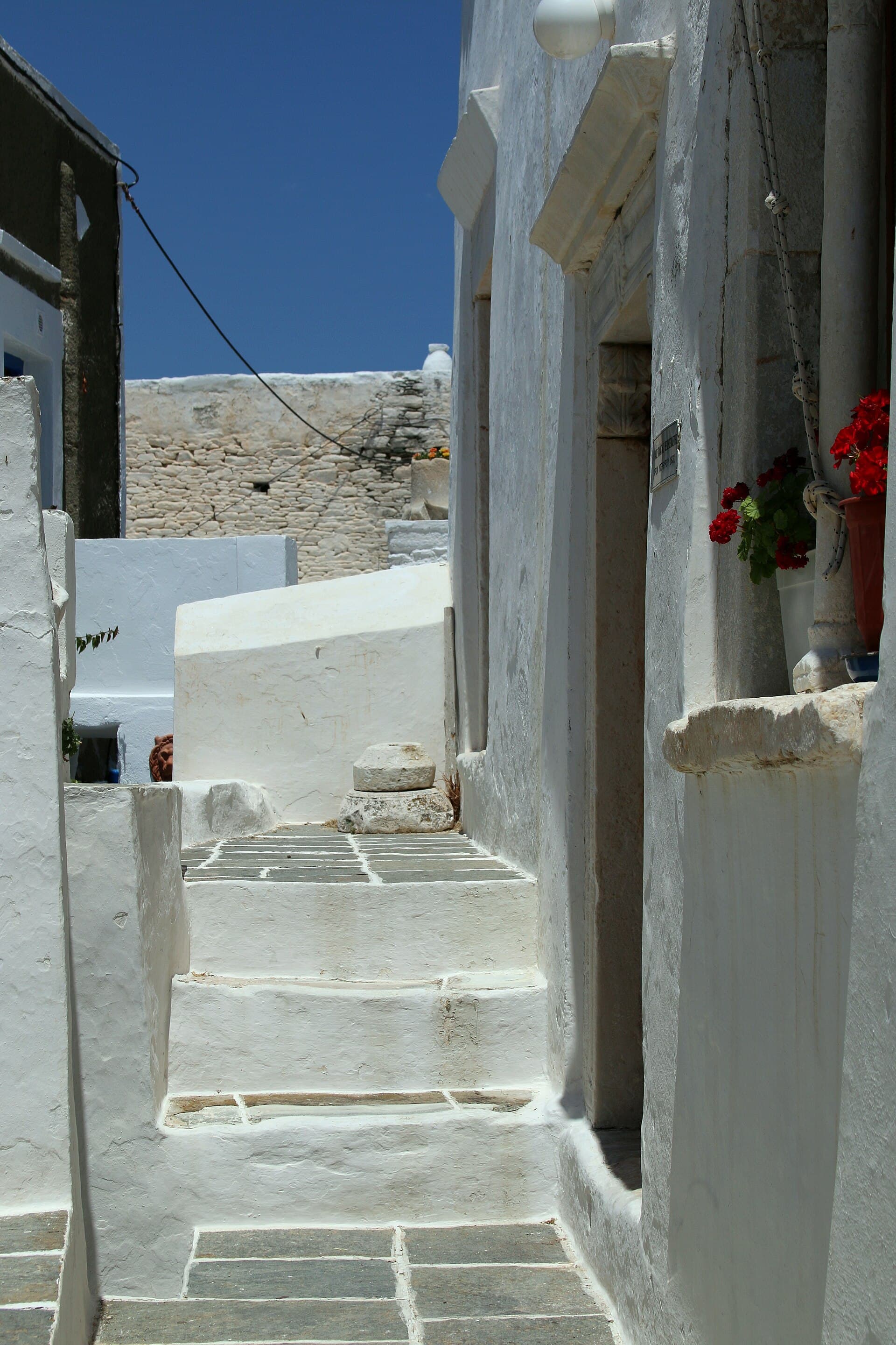 A narrow whitewashed alley with stone steps and red geraniums.